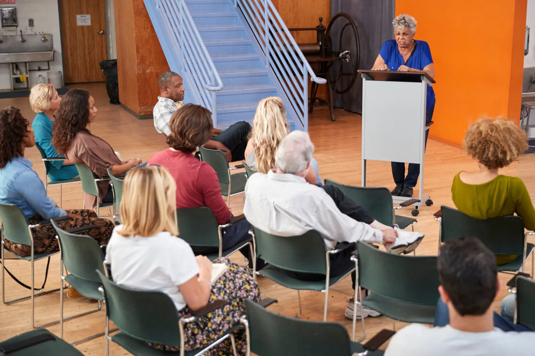 A female speaker at a podium in front of a small audience.