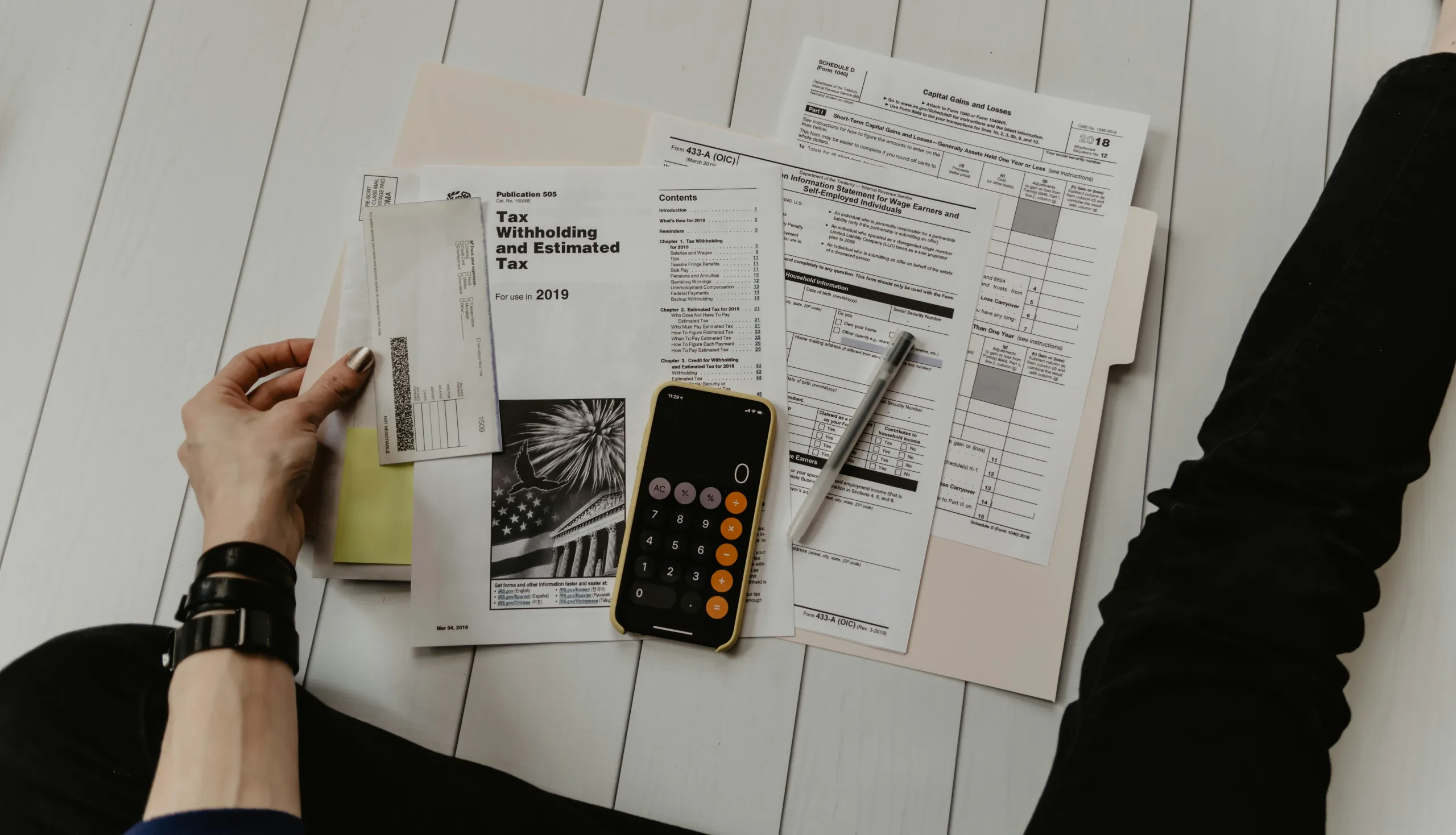Person sitting on the floor with tax forms, a calculator, pen, and check in front of them.